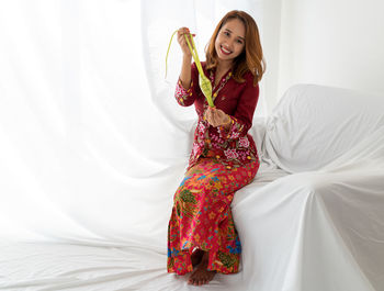 Malay lady, long hair, celebrates ramadan, in red kebaya, holding ketupat food, white background