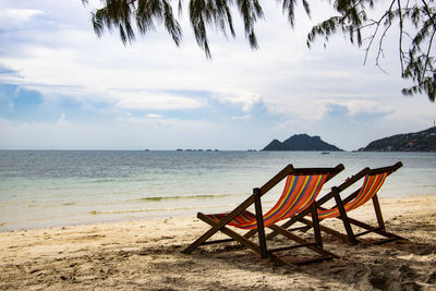 Chair on shore at beach against sky