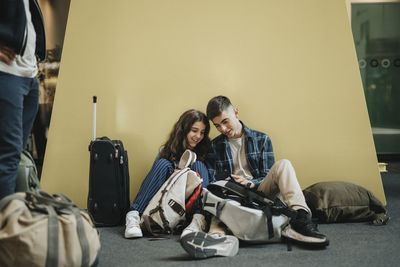 Boy sharing smart phone with sister while sitting against yellow wall