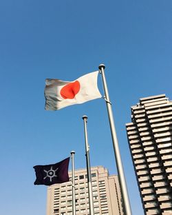 Low angle view of flag against buildings against clear blue sky