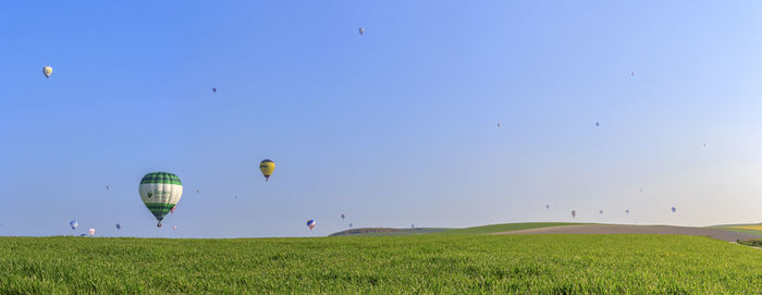 Hot air balloon flying over field against clear blue sky