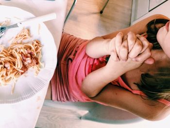 Midsection of woman with hands clasped having noodles at table