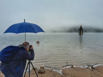 Rear view of man photographing built structure amidst lake during monsoon