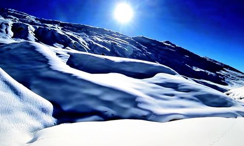 Low angle view of snow covered mountain against blue sky