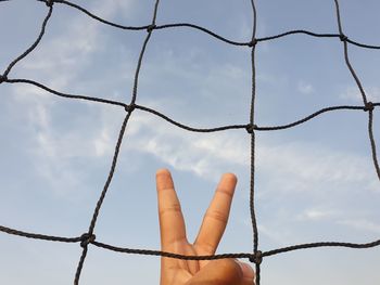 Low angle view of hand behind tennis net against sky