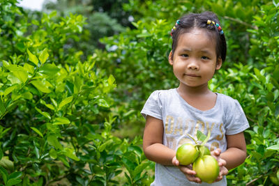 Portrait of girl holding limes while standing against plants