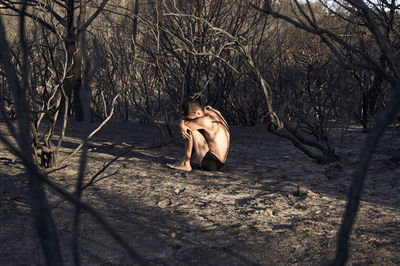 Man sitting in fetal position on burned forest floor