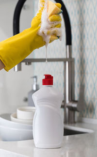 White bottle with dishwashing gel against the background of a sink and pouring foam from a sponge.