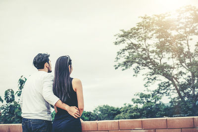 Couple standing by tree against sky