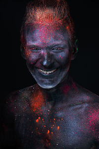 Portrait of smiling man with powdered paint against black background