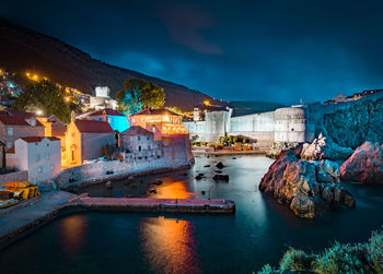 Illuminated buildings by sea against sky at night