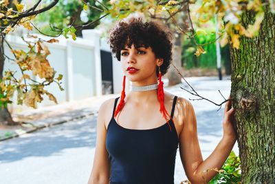 Portrait of beautiful young woman standing by tree trunk