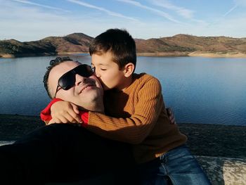 Boy kissing father against lake