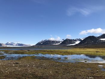 Scenic view of lake and snowcapped mountains against blue sky