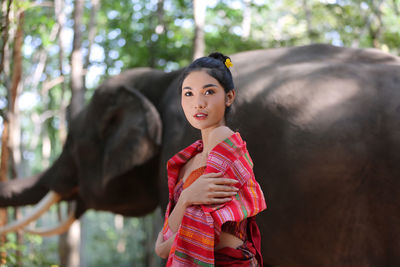 Thoughtful woman looking away while standing against elephant