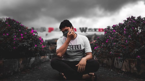 Full length of young man sitting on plants against sky