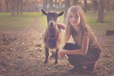 Portrait of girl crouching by goat on field