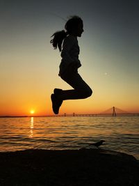 Side view full length of girl jumping by sea with bandraworli sea link in background during sunset