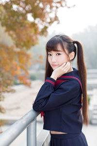 Portrait of young woman with long hair standing by railing