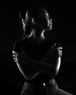 Side view of young woman standing against black background