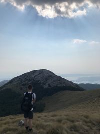 Rear view of man standing on mountain against sky