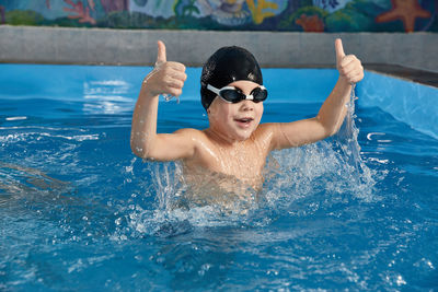 Preschool boy learning how to swim in a pool wearing swimming cap and goggles