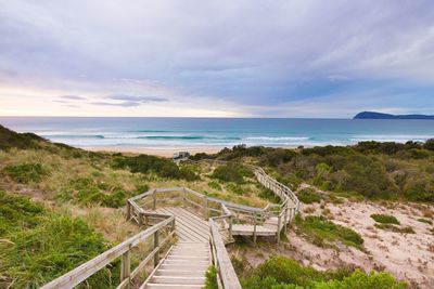 Boardwalk on beach against cloudy sky 