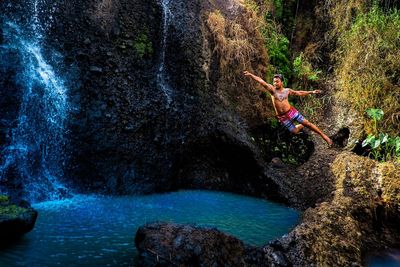 Man jumping in pond by waterfall