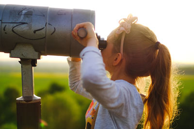 Side view of girl looking through coin-operated binoculars