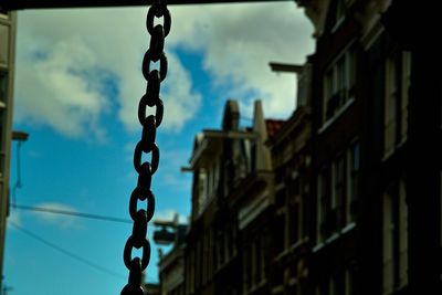 Low angle view of chain hanging amidst buildings against sky