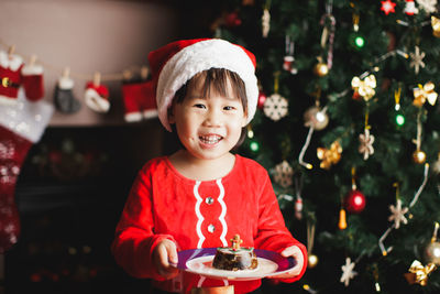 Portrait of smiling girl holding food on plate against christmas tree