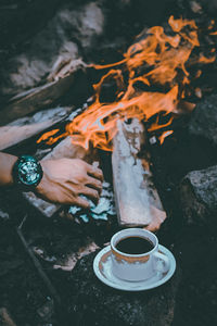 Cropped hand of man over coffee by bonfire