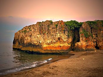 Rock formation on beach against sky during sunset