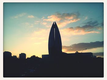 Silhouette of buildings against cloudy sky during sunset