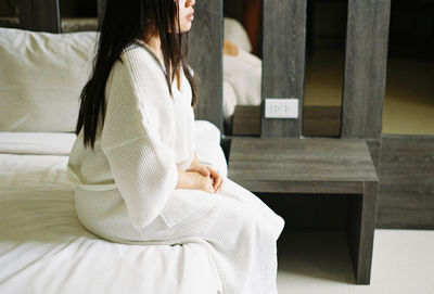 Midsection of young woman sitting on bed at home