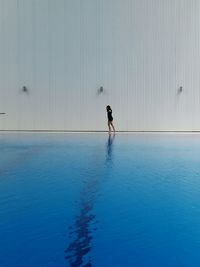 Woman walking by swimming pool against wall