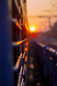 Close-up of illuminated lighting equipment on railing against sky during sunset