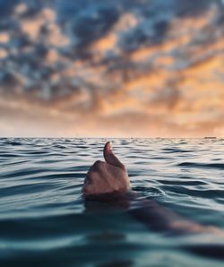 Cropped hand of person gesturing in sea during sunset