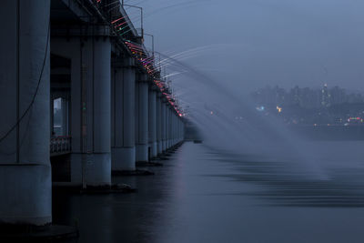 Low angle view of water flowing from bridge in river against sky at dusk