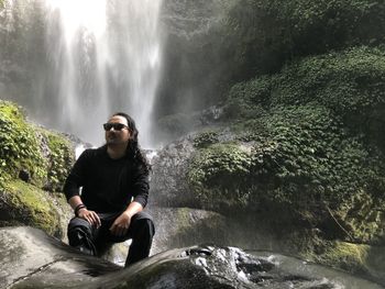 Full length of man sitting on rock against waterfall