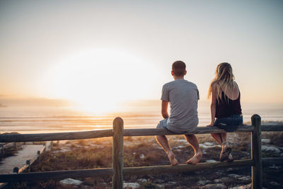 Rear view of couple sitting on railing against beach