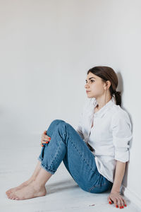 Young woman looking away while sitting on wall