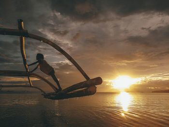 Girl standing on outrigger over sea during sunset