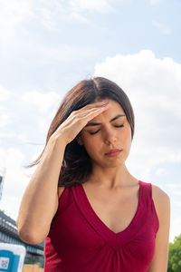 Low angle view of woman with headache standing against sky