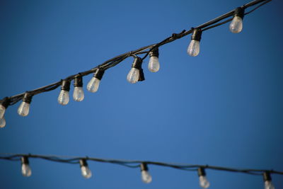 Low angle view of lighting equipment hanging against clear blue sky