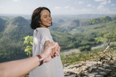 Smiling young woman standing on landscape against mountains