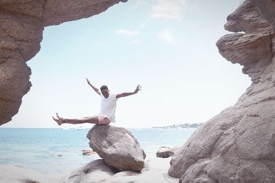 Man standing on rock by sea against sky