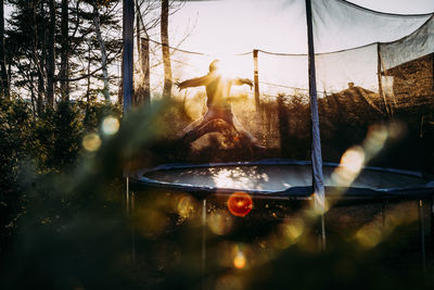 Young boy jumping on trampoline in a star position during golden hour