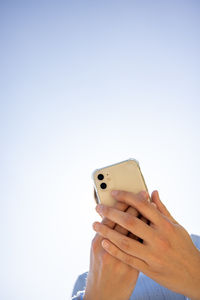 Cropped hands of woman using mobile phone against clear sky