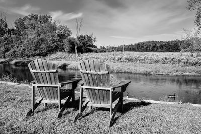 Empty chairs by lake against sky